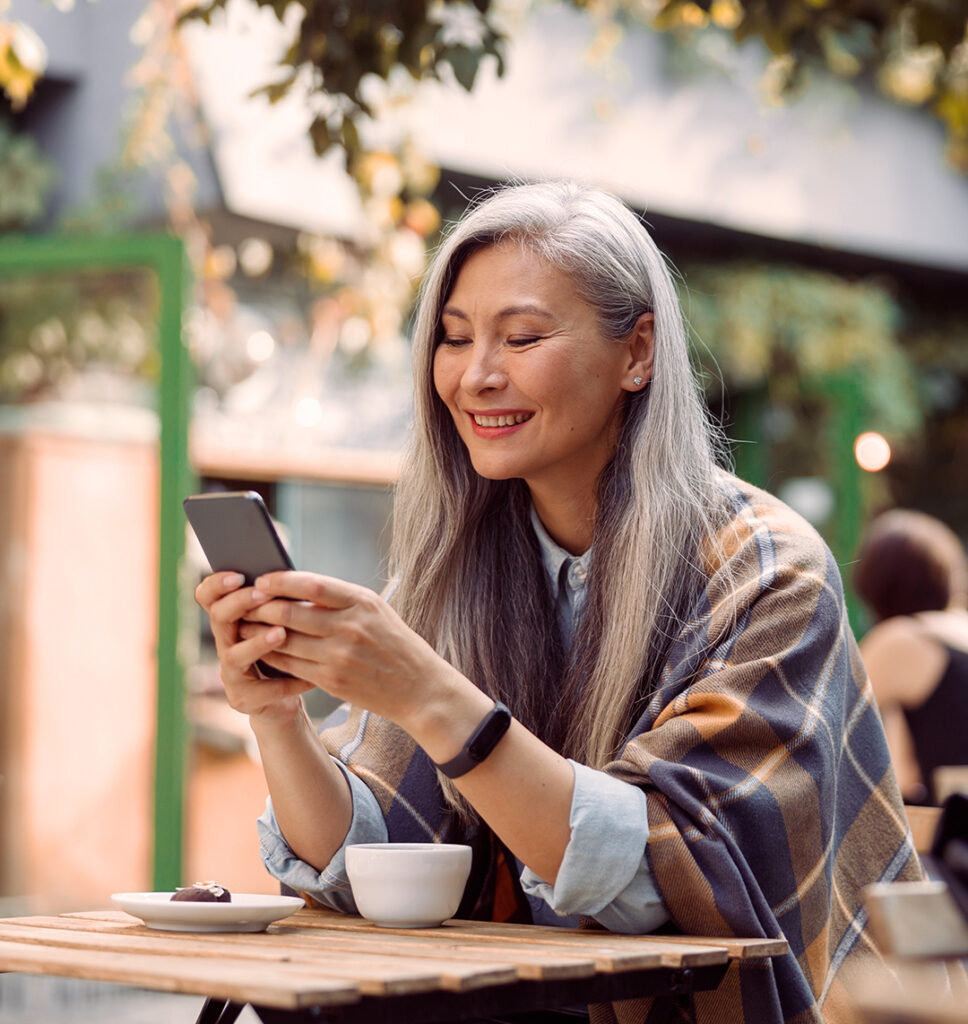 Eine Frau im mittleren Alter schaut freudig lächelnd auf ihr Smartphone.