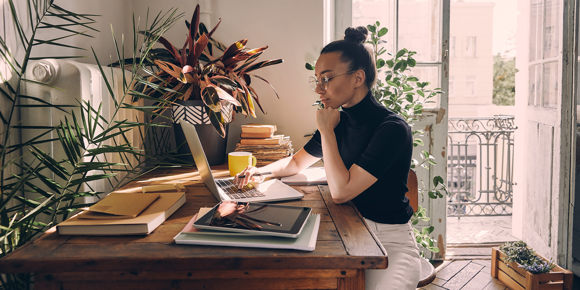 Eine junge Frau sitzt Zuhause am Schreibtisch und arbeitet am Laptop.