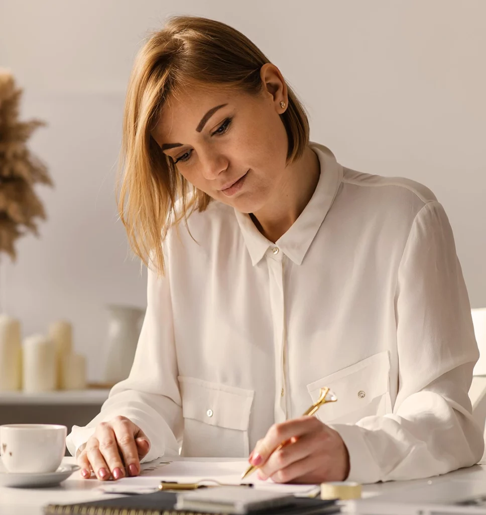 Eine Frau sitzt am Schreibtisch und schaut konzentriert auf das Papier vor ihr.