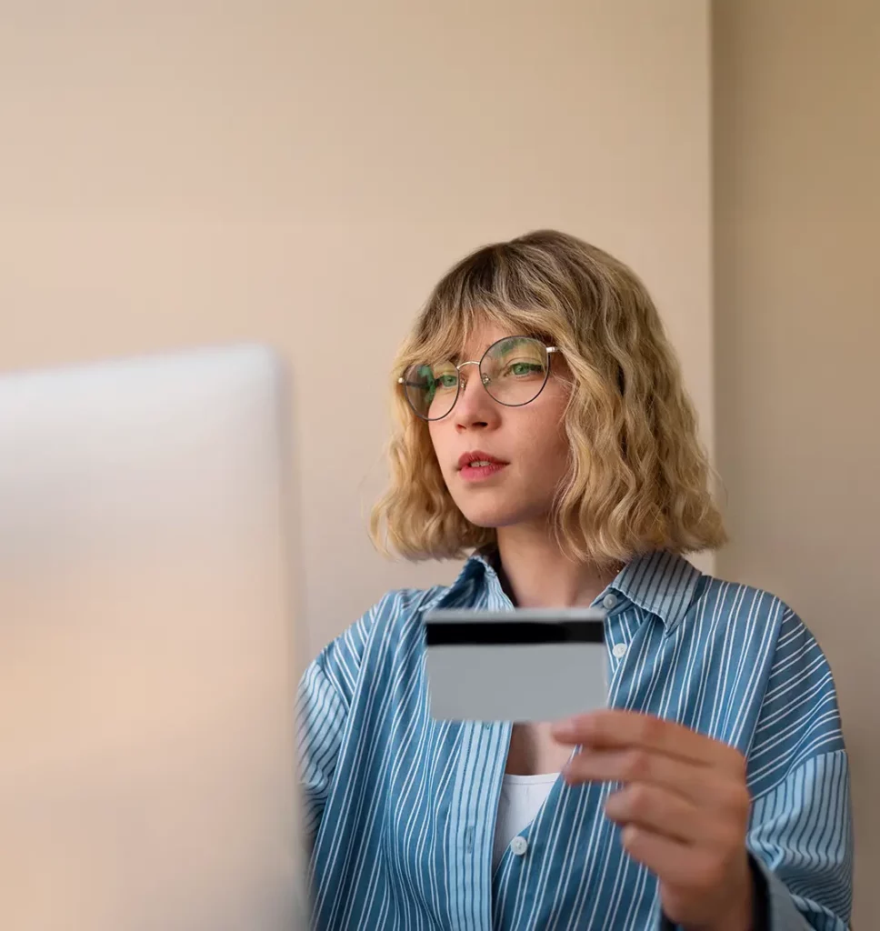 Junge Frau sitzt mit einer Kreditkarte in der Hand vor einem Computer und zahlt direkt